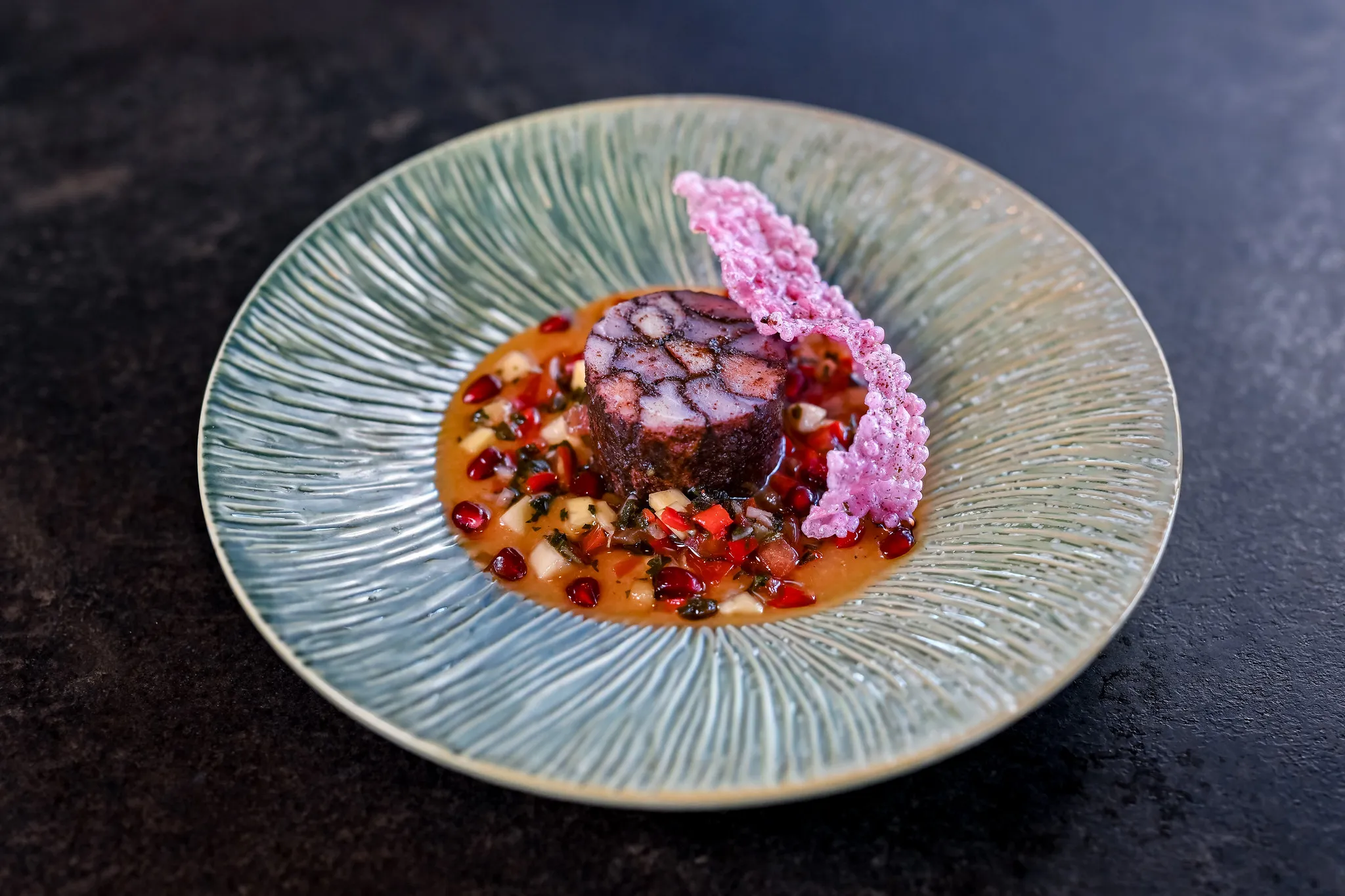 Oktopussteak mit Granatapfelvinaigrette auf handgemachtem Keramikteller.