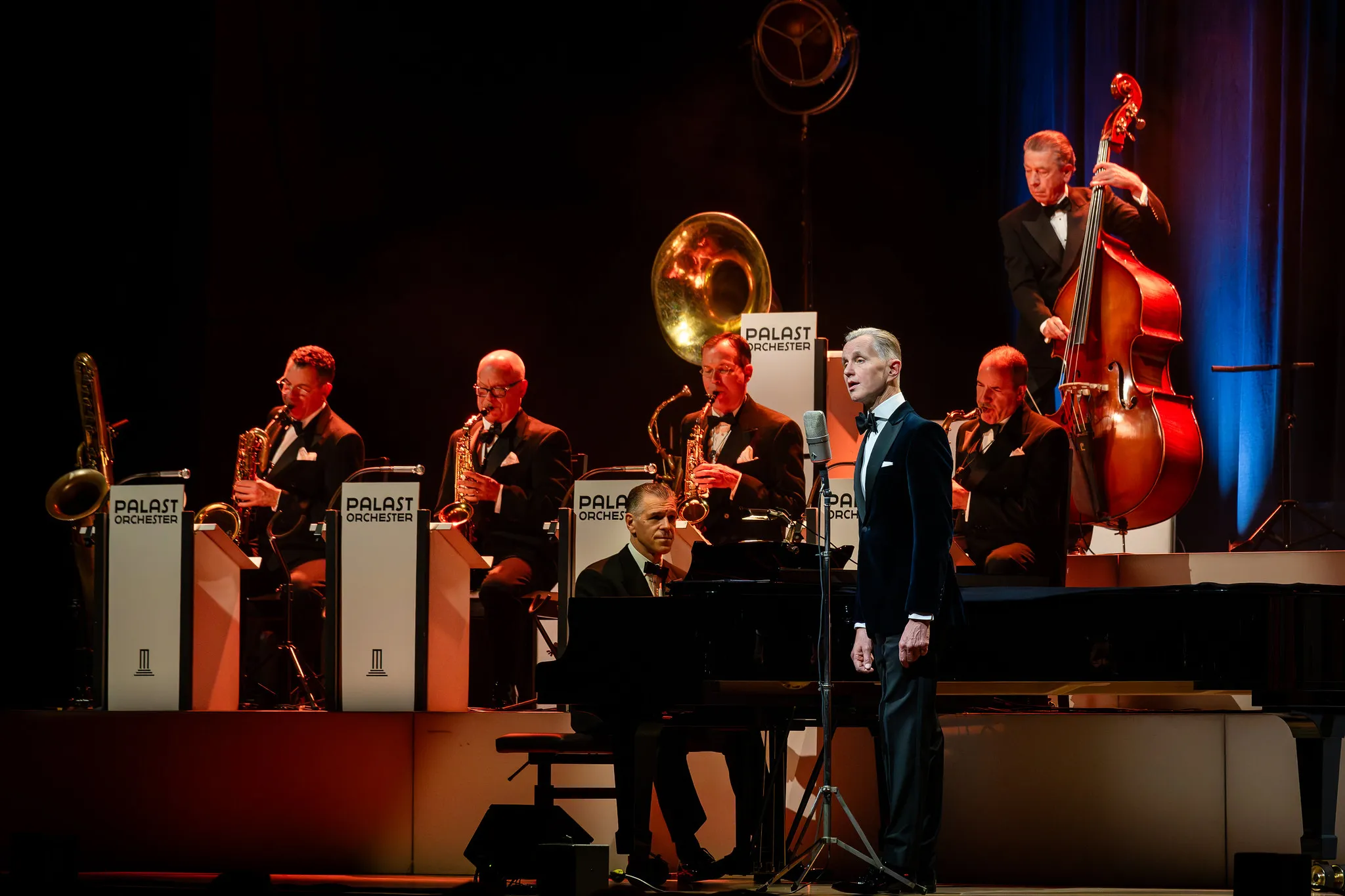 Palast Orchester auf der Bühne: Saxofonisten, Kontrabass und Solist am Mikrofon, Konzertfotografie der Big-Band-Besetzung.