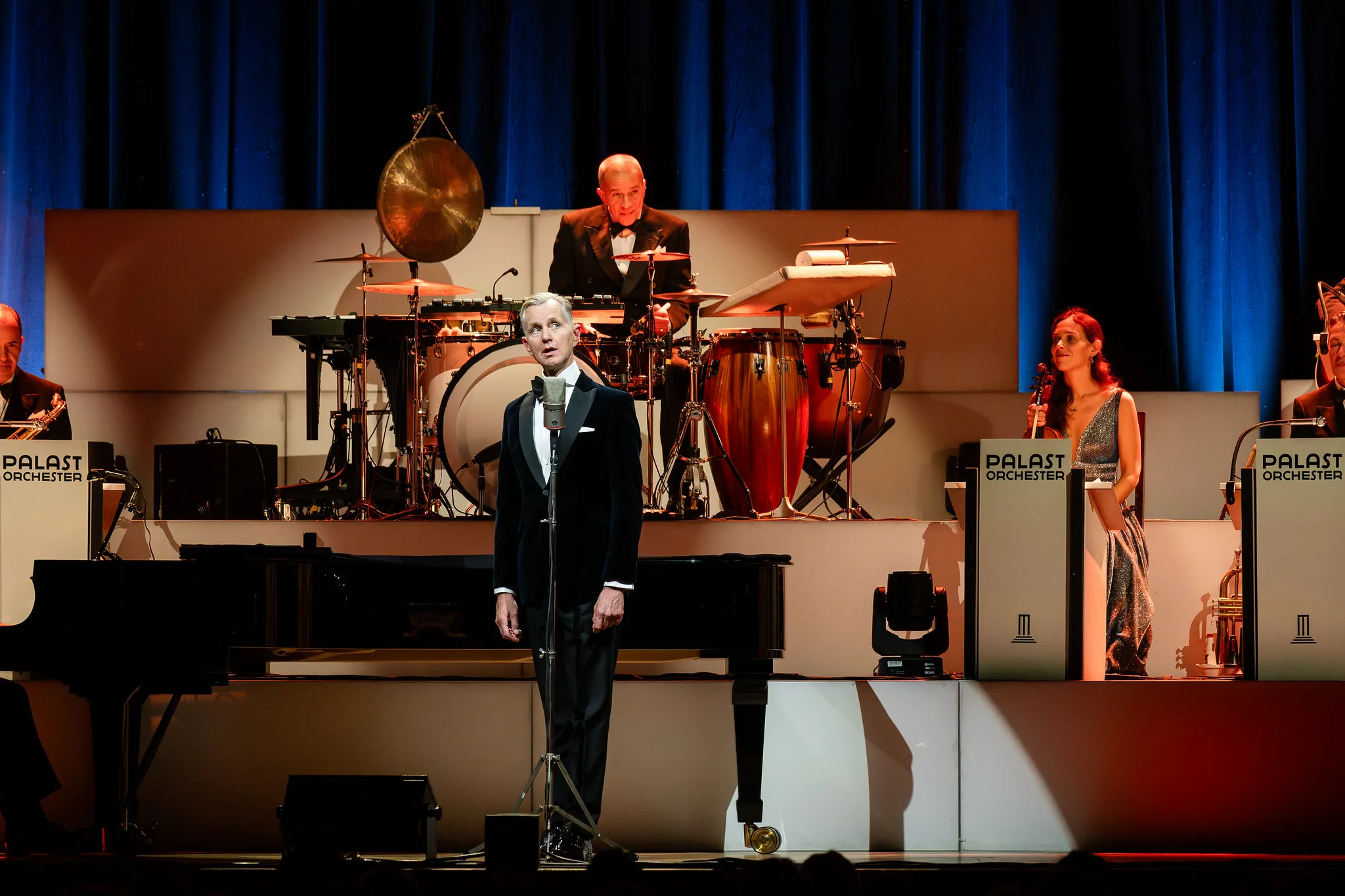 Sänger im Smoking am Vintage-Mikrofon, das Palast Orchester mit Drums und Piano im Hintergrund, Kulturfotografie Nürnberg.