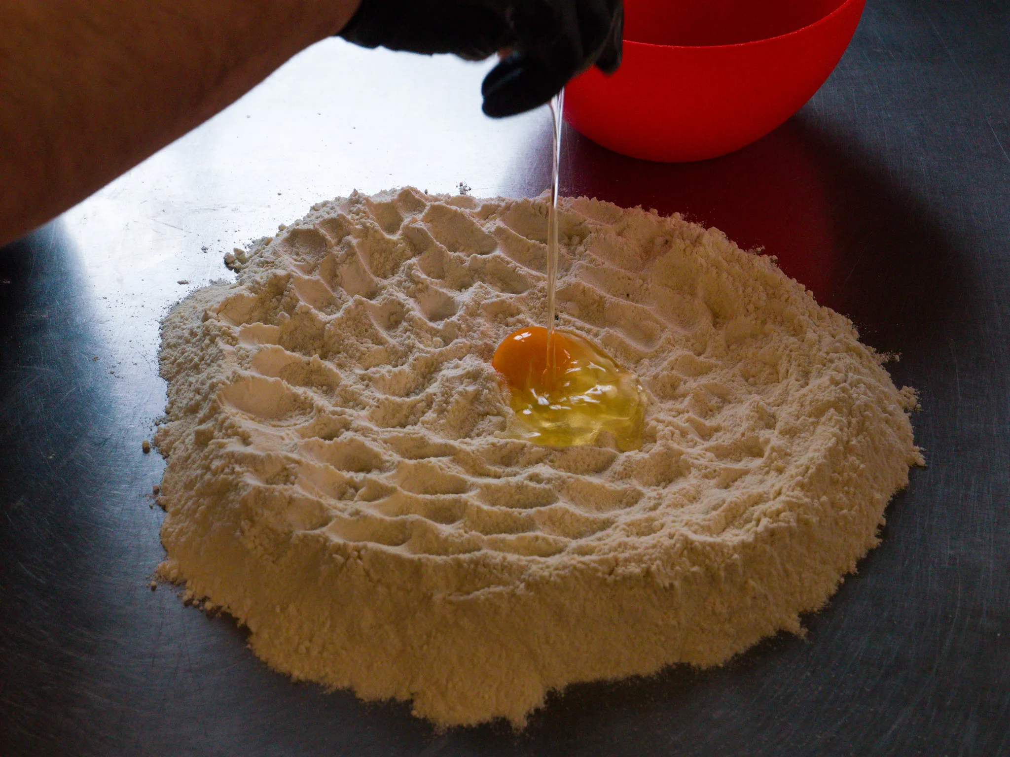 Ei in Mehlkrater auf Edelstahlarbeitsplatte, handgemachte Pasta-Vorbereitung.
