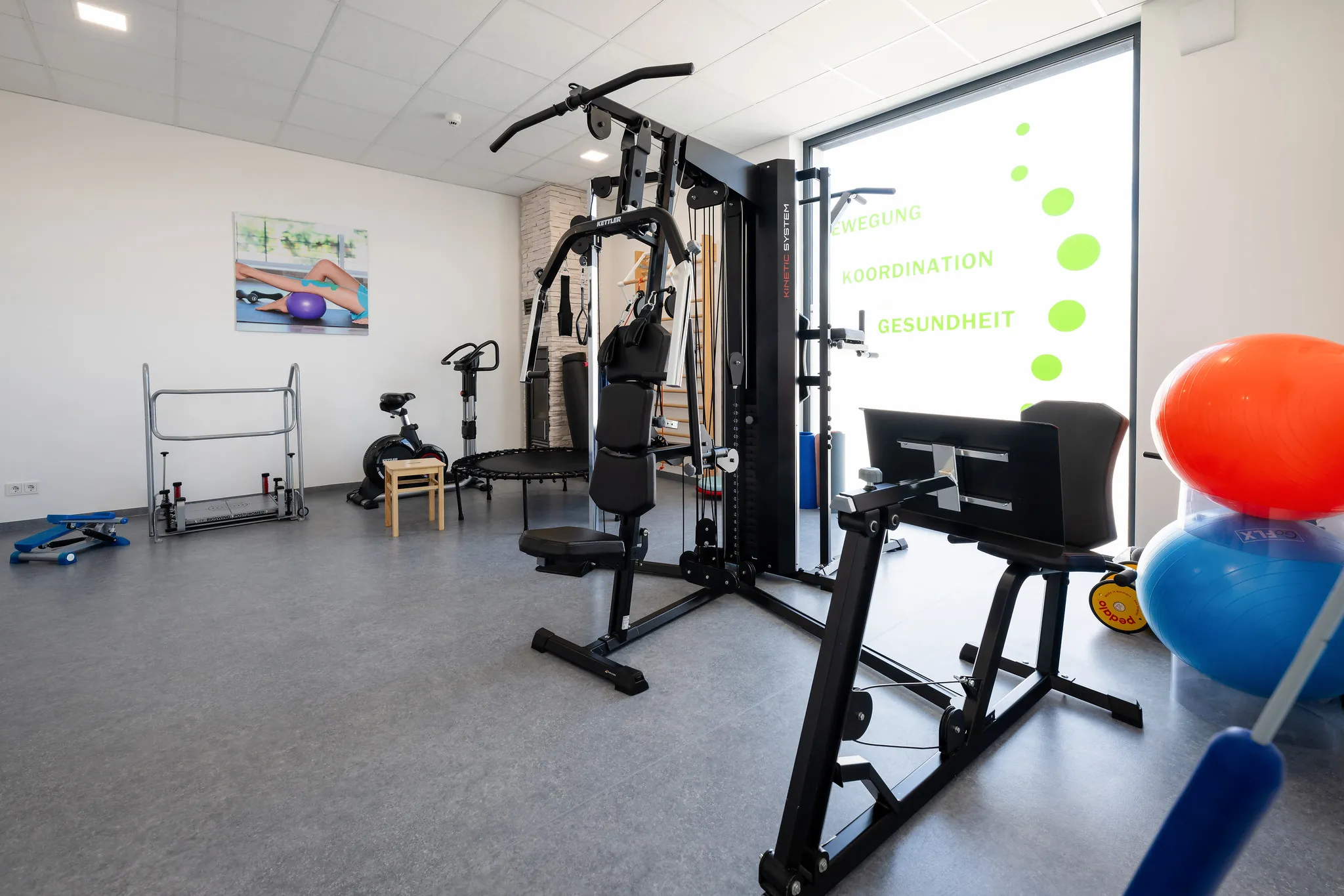 Physiotherapie-Trainingsraum mit Geräten und Gymnastikbällen.