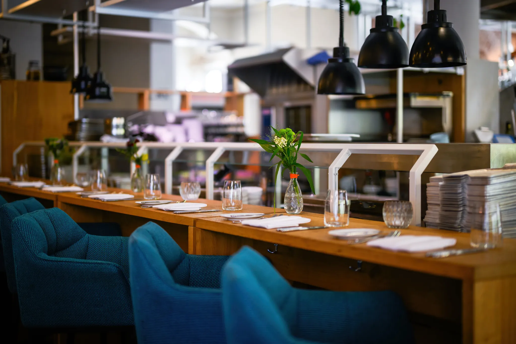 Eingedeckter Chef's Table an der offenen Küche mit petrolfarbenen Sesseln, Restaurantfotografie Nürnberg.