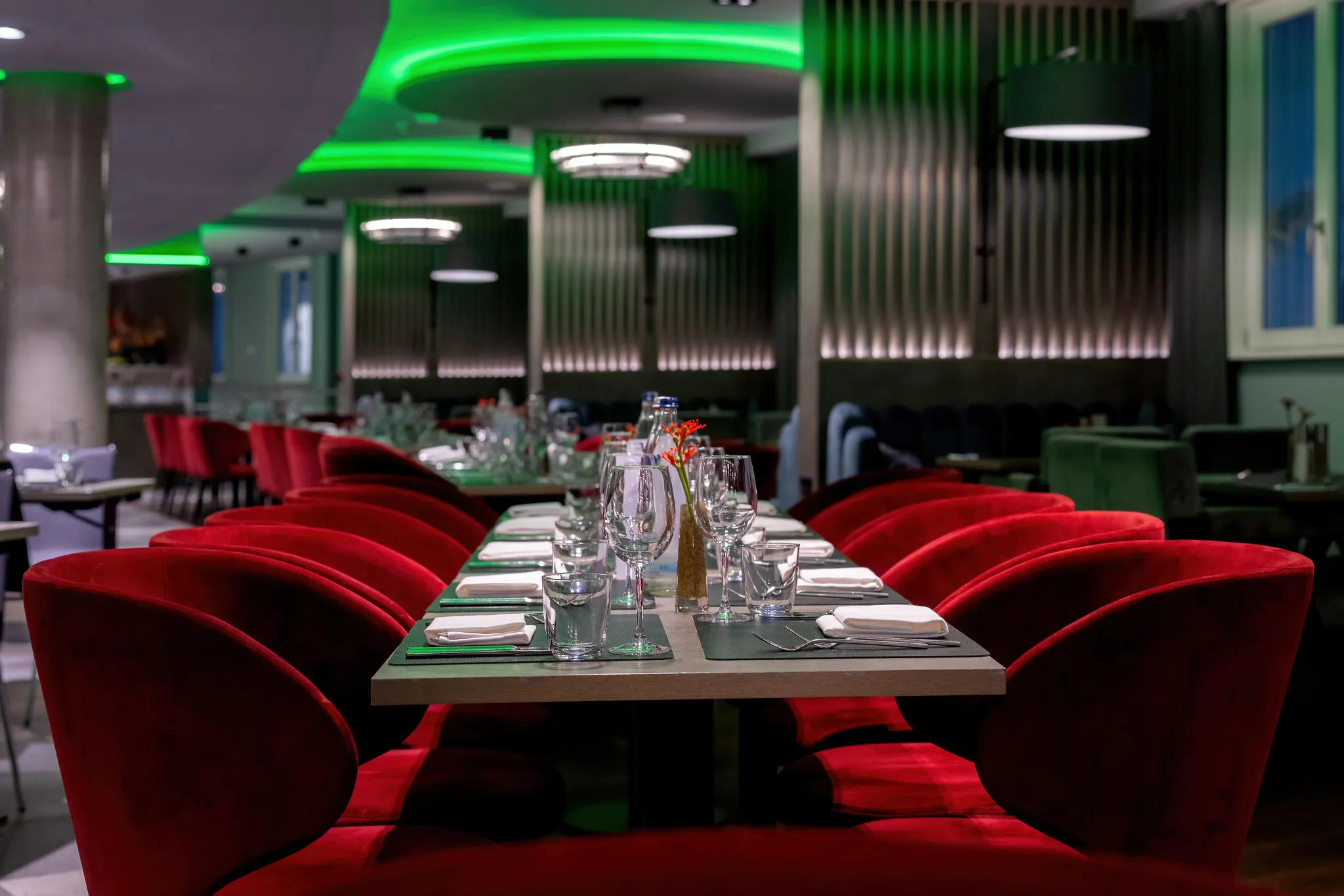 Restaurant mit roten Samtstühlen und grünem Ambientelicht.