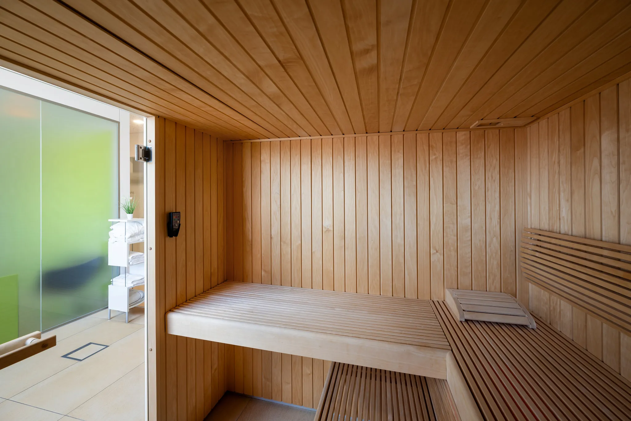Sauna aus hellem Holz mit Glastür.