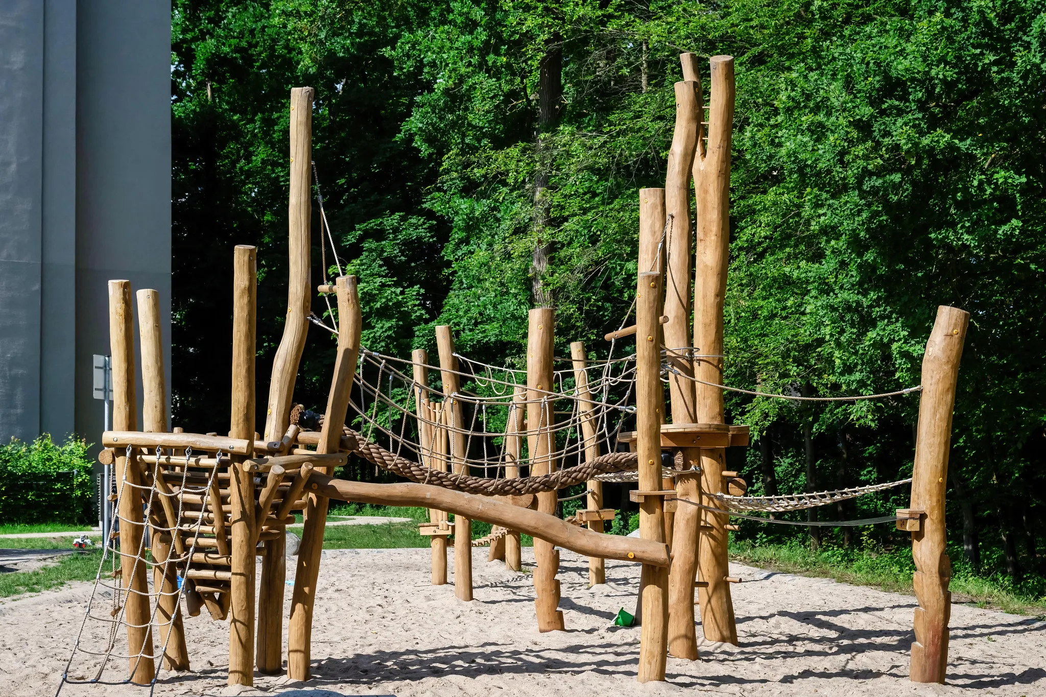 Spielplatz mit Holz-Klettergerüst und Seilbrücke am Waldrand.