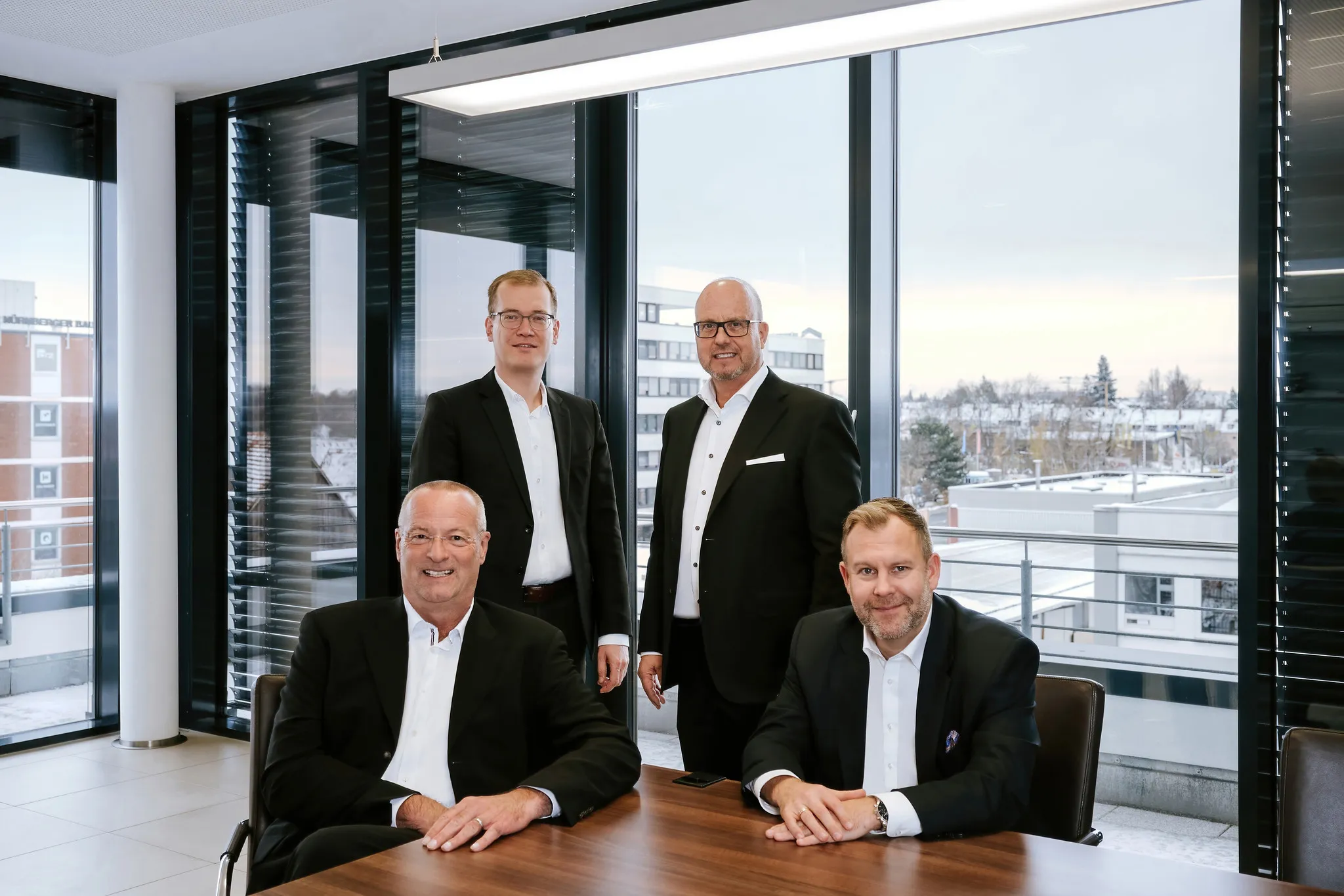 Vier Geschäftsmänner im Anzug als Team-Portrait am Fenster, gemeinsames Business-Portrait