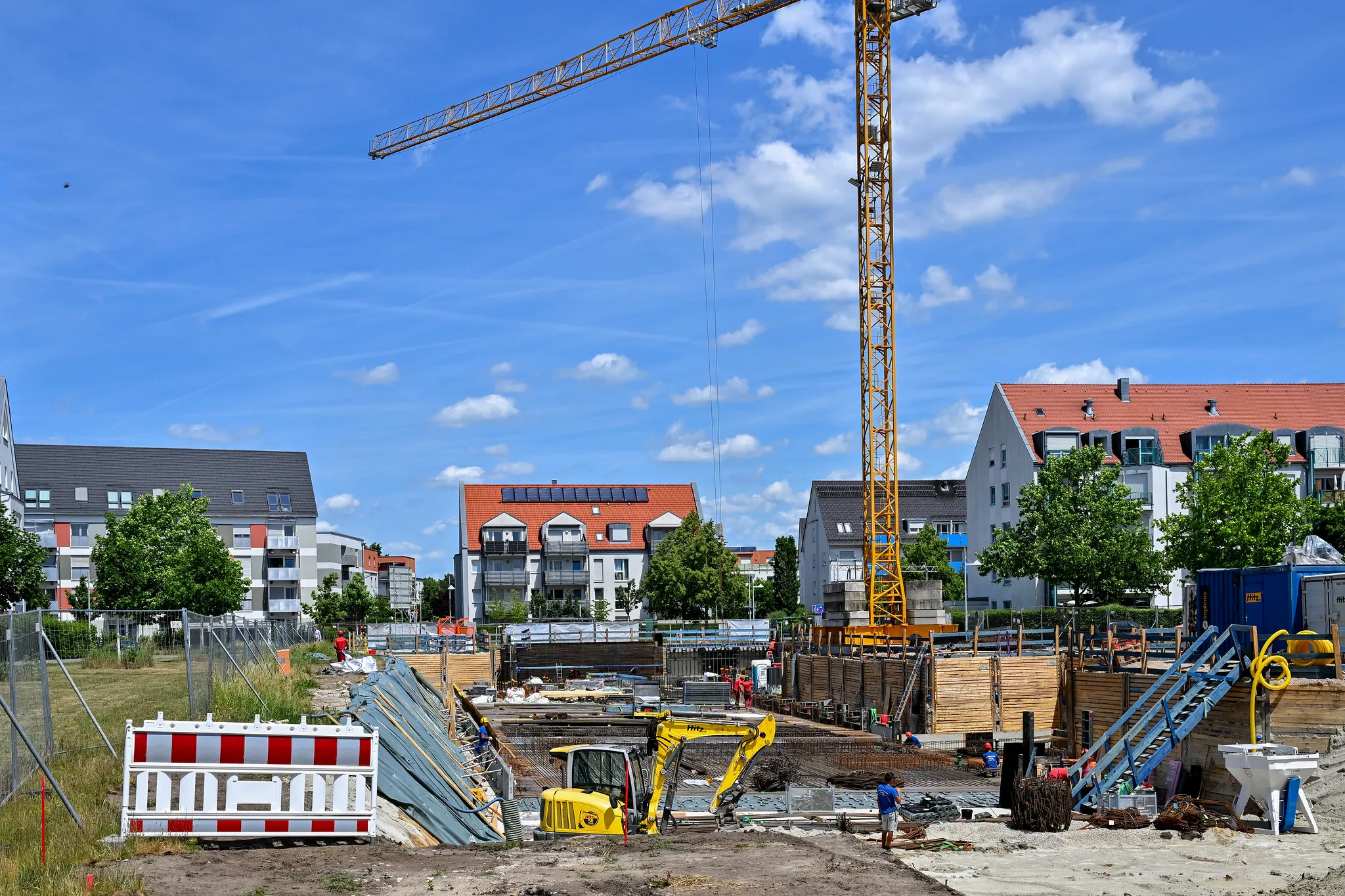 Aktive Wohnbau-Baustelle mit Bagger und Kran, Fundamentarbeiten im Gange