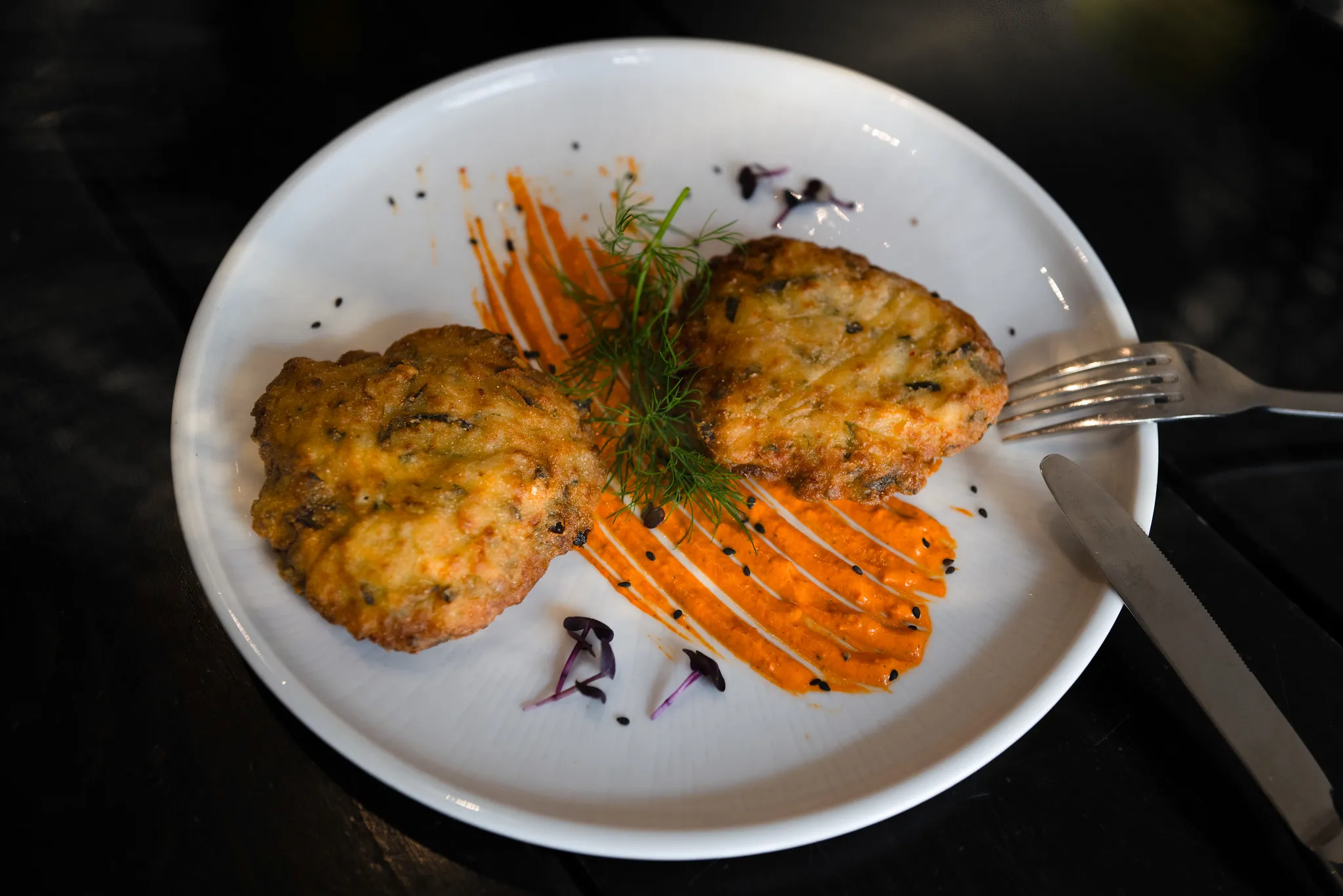 Zwei knusprige Zucchini-Fritter mit Karottensoße und frischem Dill.