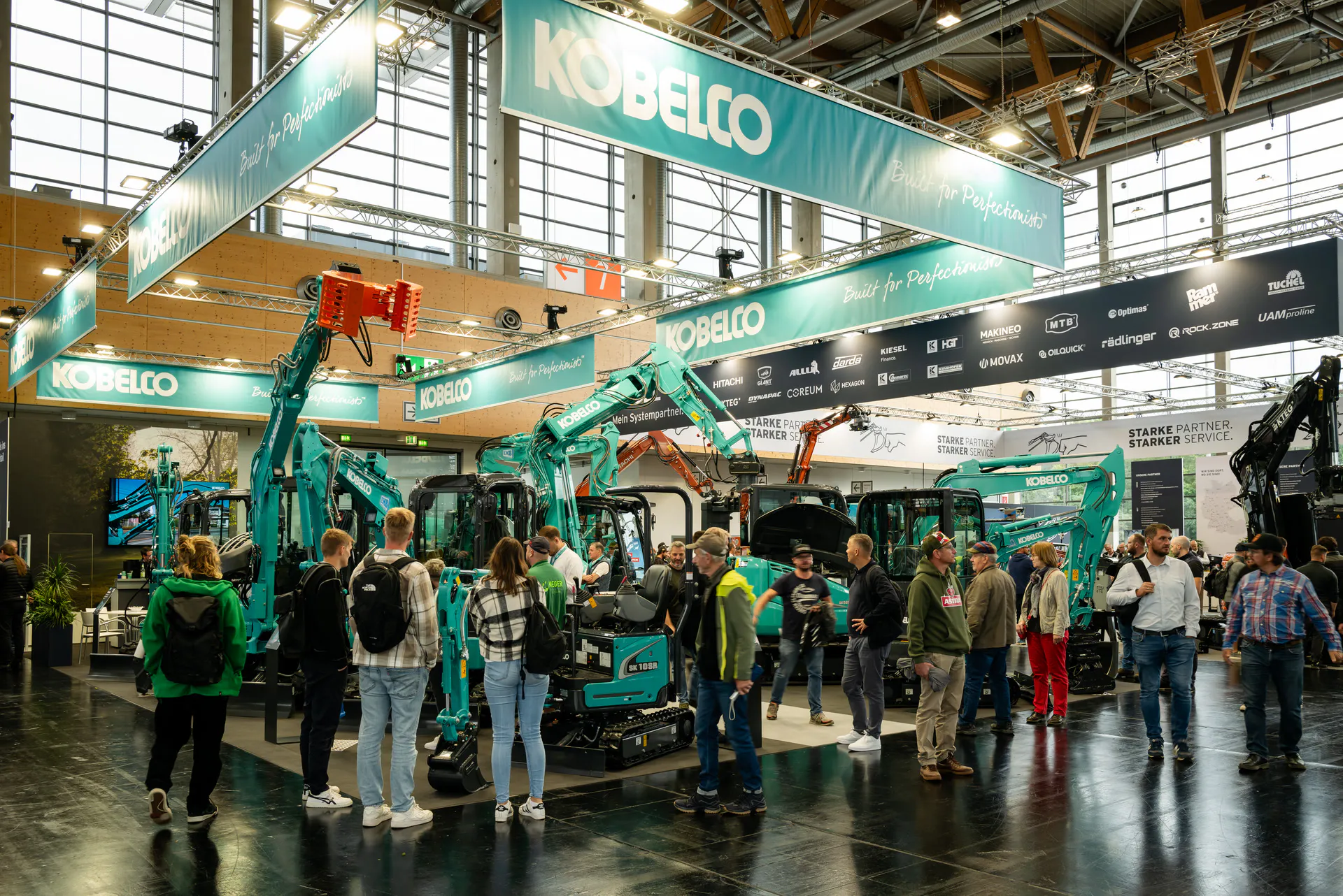 Large Kobelco brand stand with excavators and trade visitors in a hall at GaLaBau in Nuremberg, photographed by the trade fair photographer