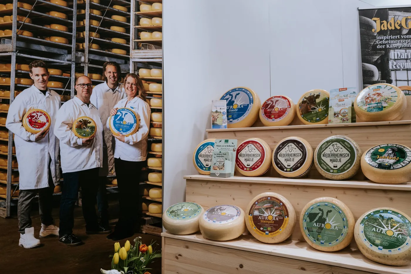 Booth team in white coats in front of cheese wheels